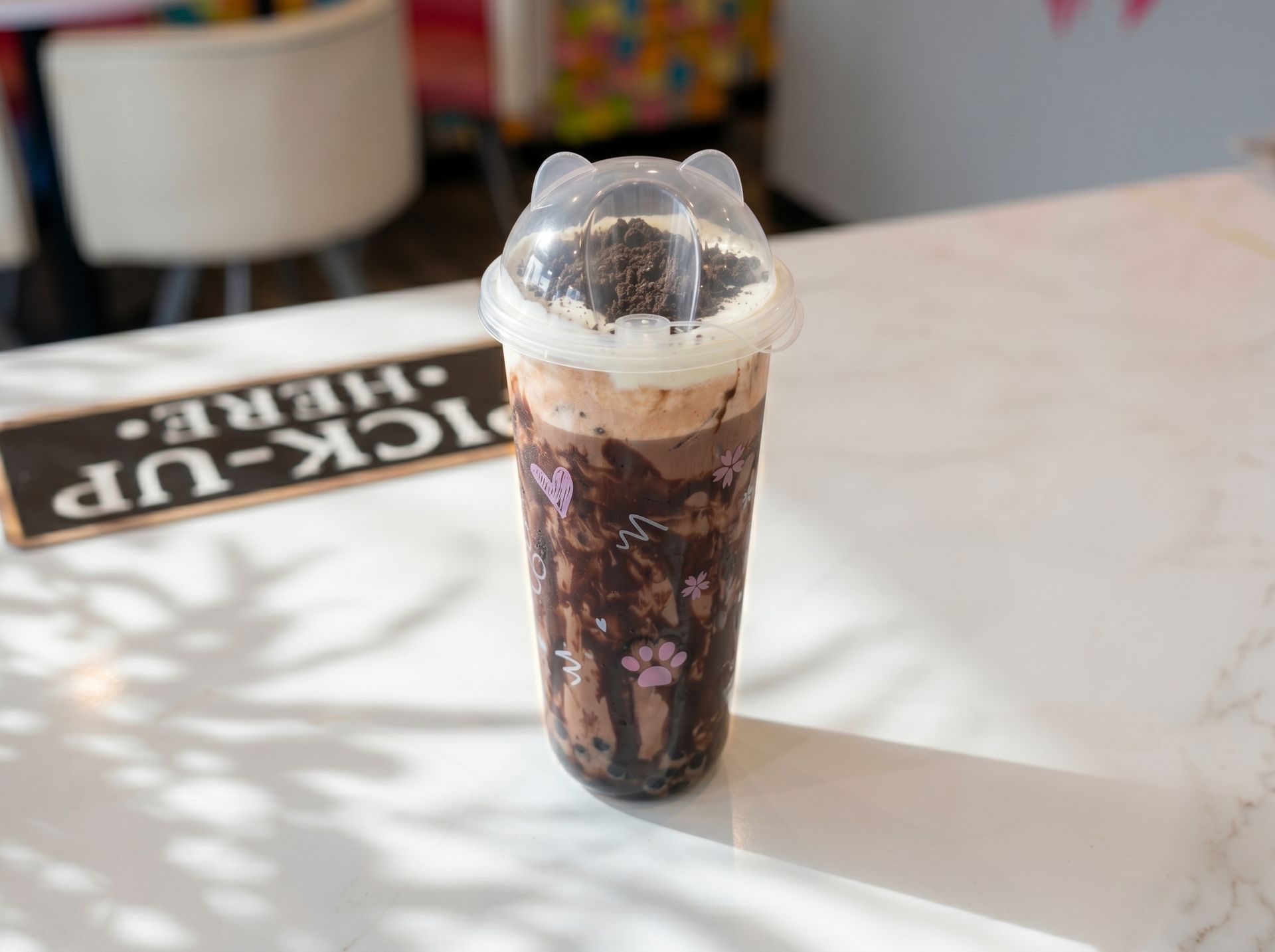 Tall plastic cup of dark iced drink with cream foam on a bright café table