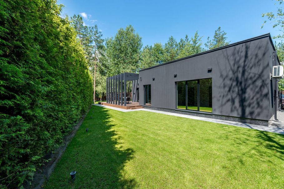White two-story house with large windows, landscaped flower beds, and tall trees in the yard