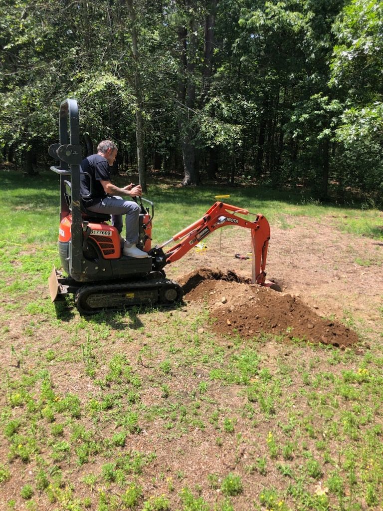 Person operating a mini excavator digging soil in a grassy yard near trees