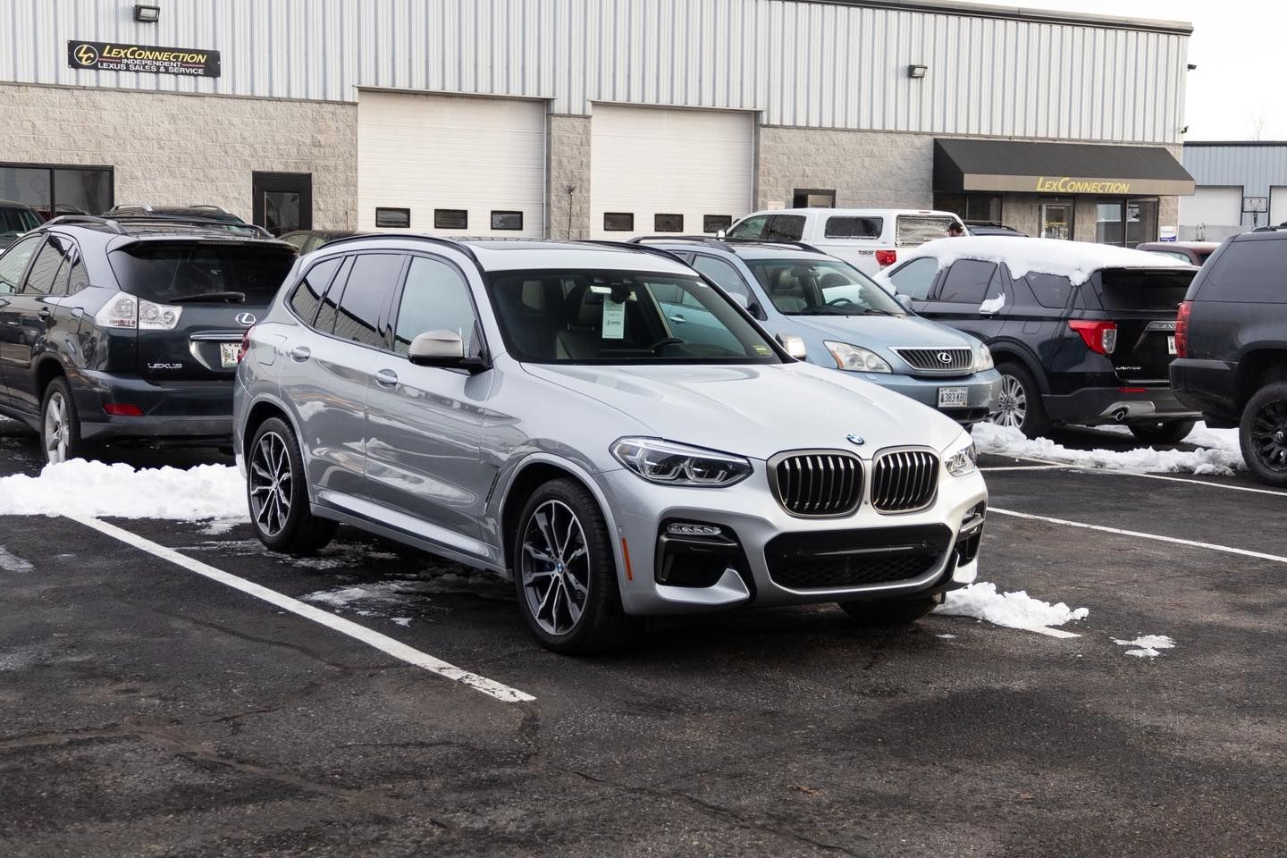 Silver BMW SUV parked in a snowy lot outside a dealership building