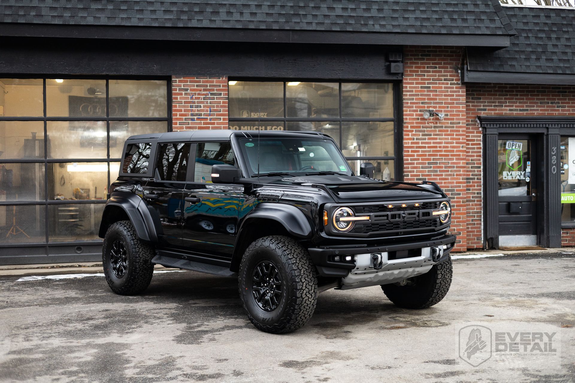 Black Ford Bronco parked outside a brick building with large windows.