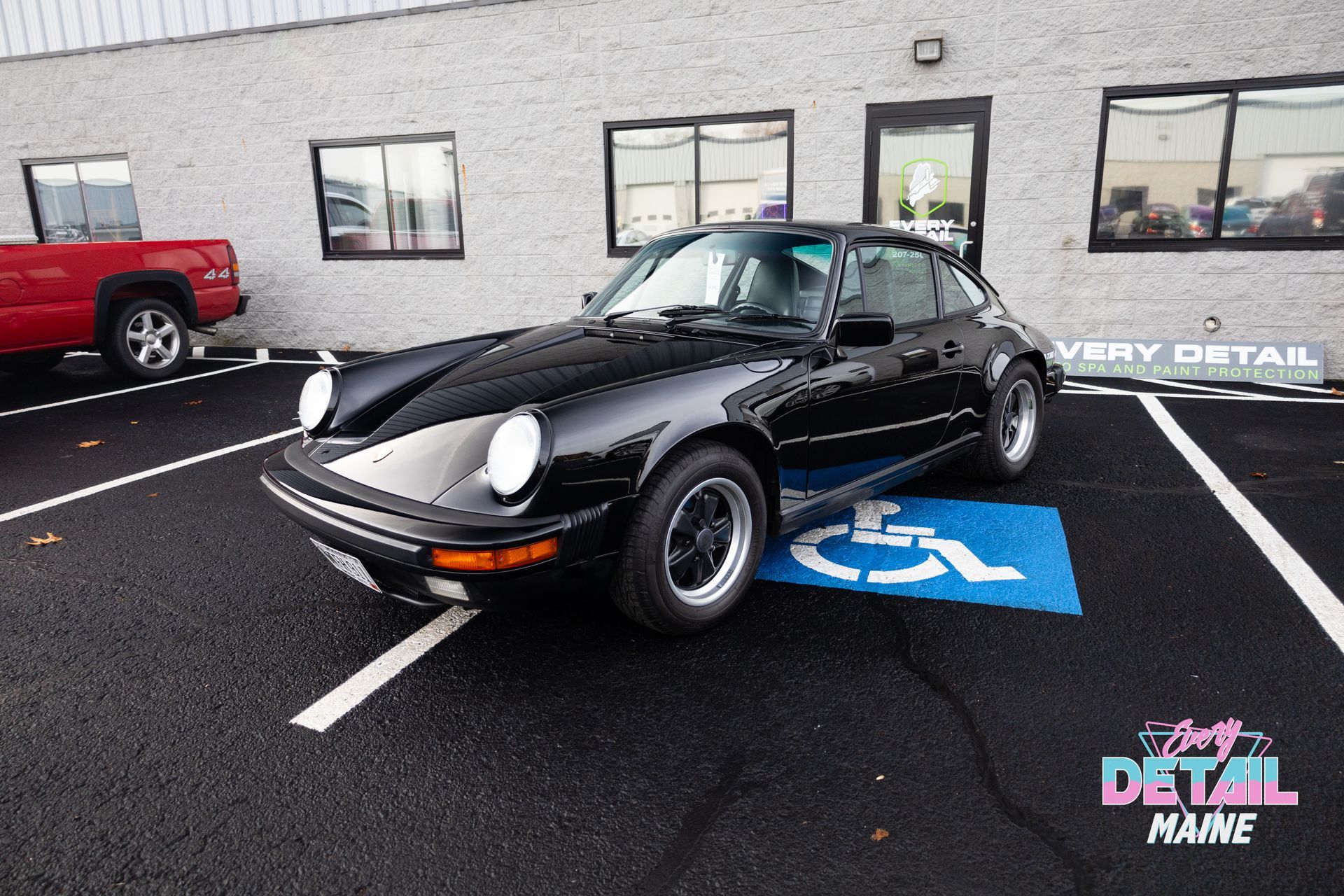 Black Porsche 911 parked in a handicap parking spot in front of a building.