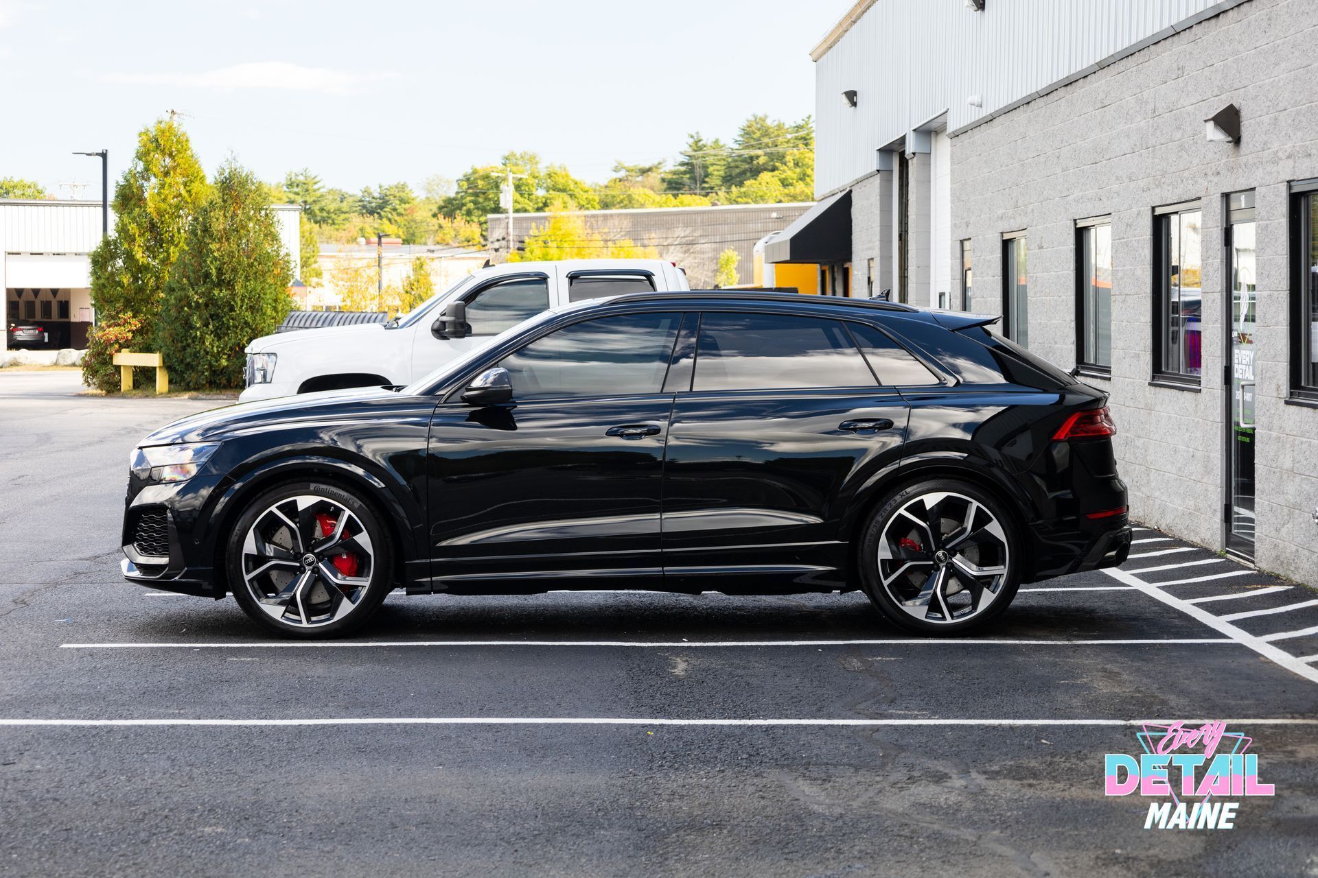 A black car is parked in a parking lot in front of a building.