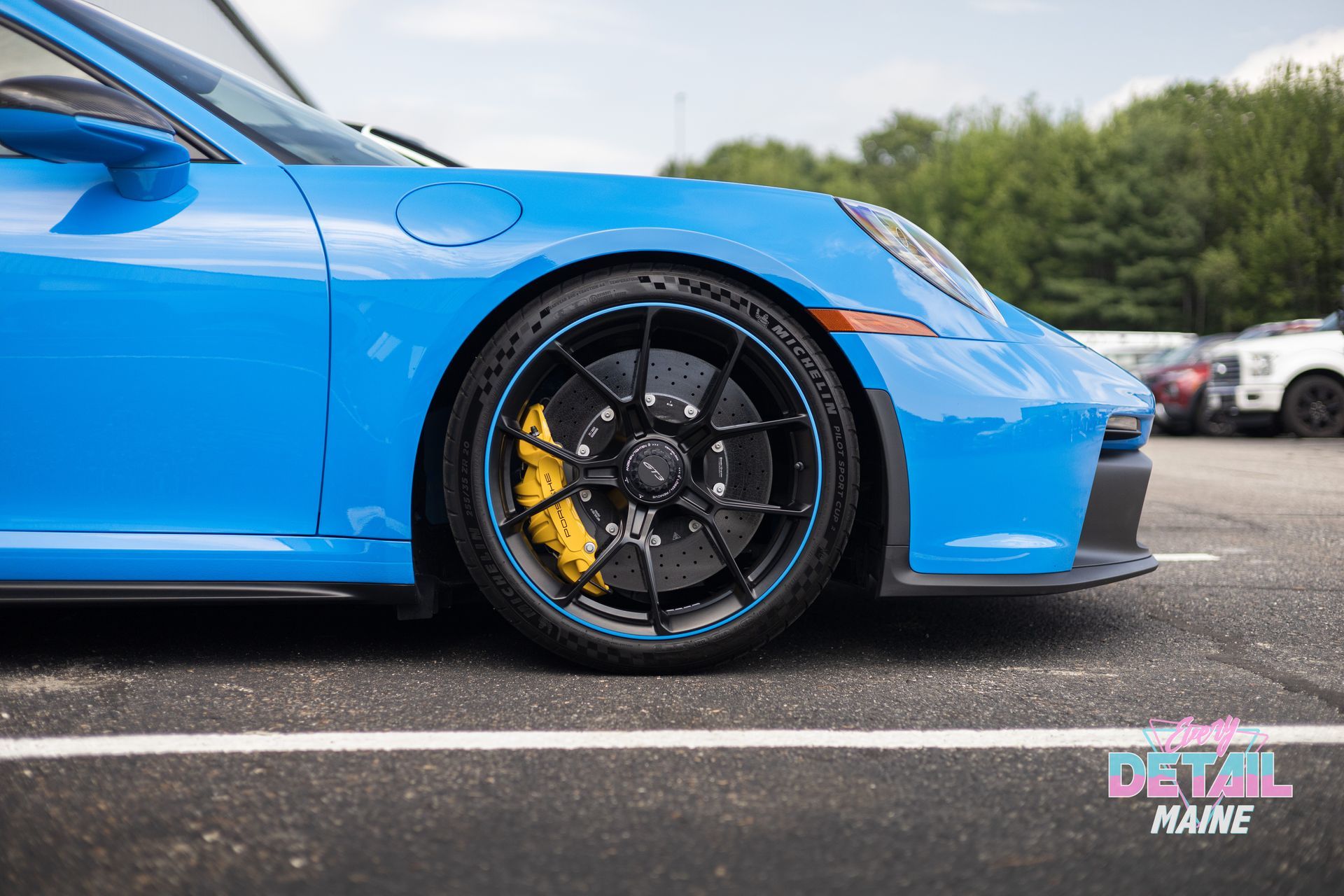 Man cleaning a bright blue Porsche sports car; garage setting.