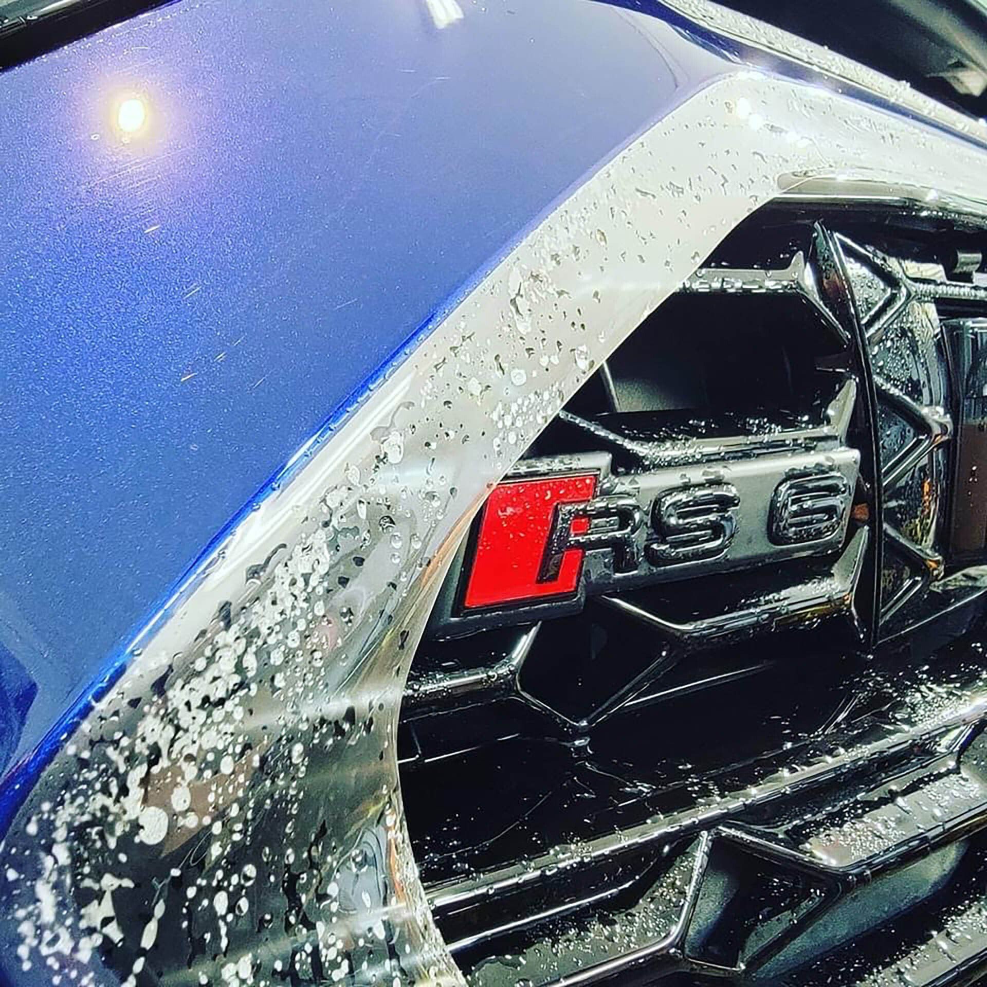 Close-up of an Audi RS 6 emblem on a blue car with soap suds.