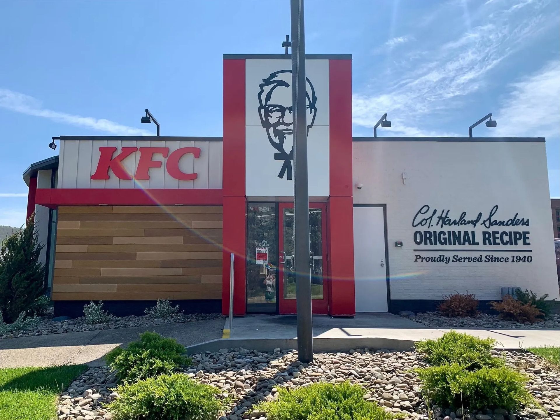 KFC restaurant exterior with red-and-white signage and Colonel Sanders logo under a blue sky