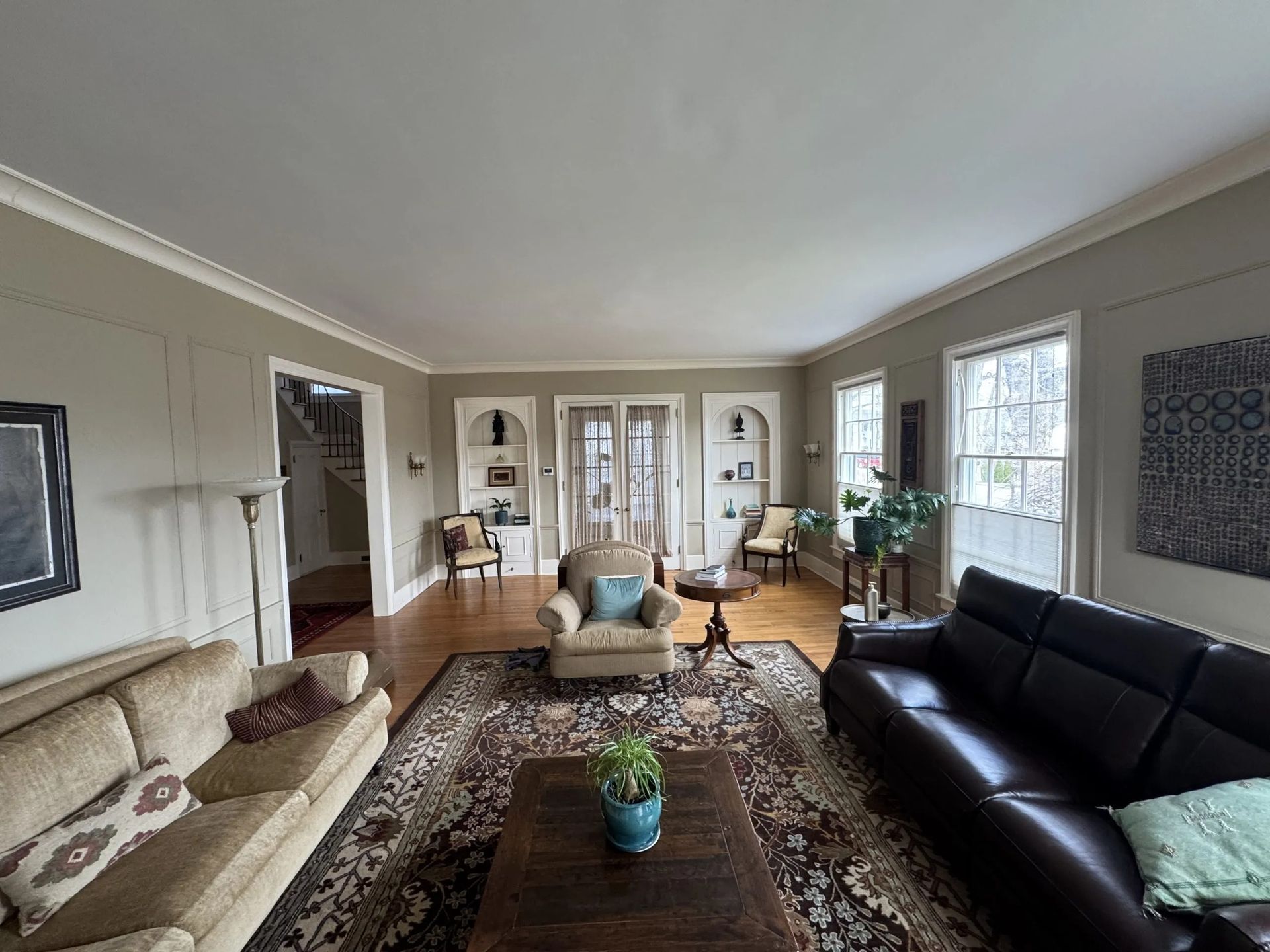 Bright living room with beige and black sofas, patterned rug, chairs, and large windows.