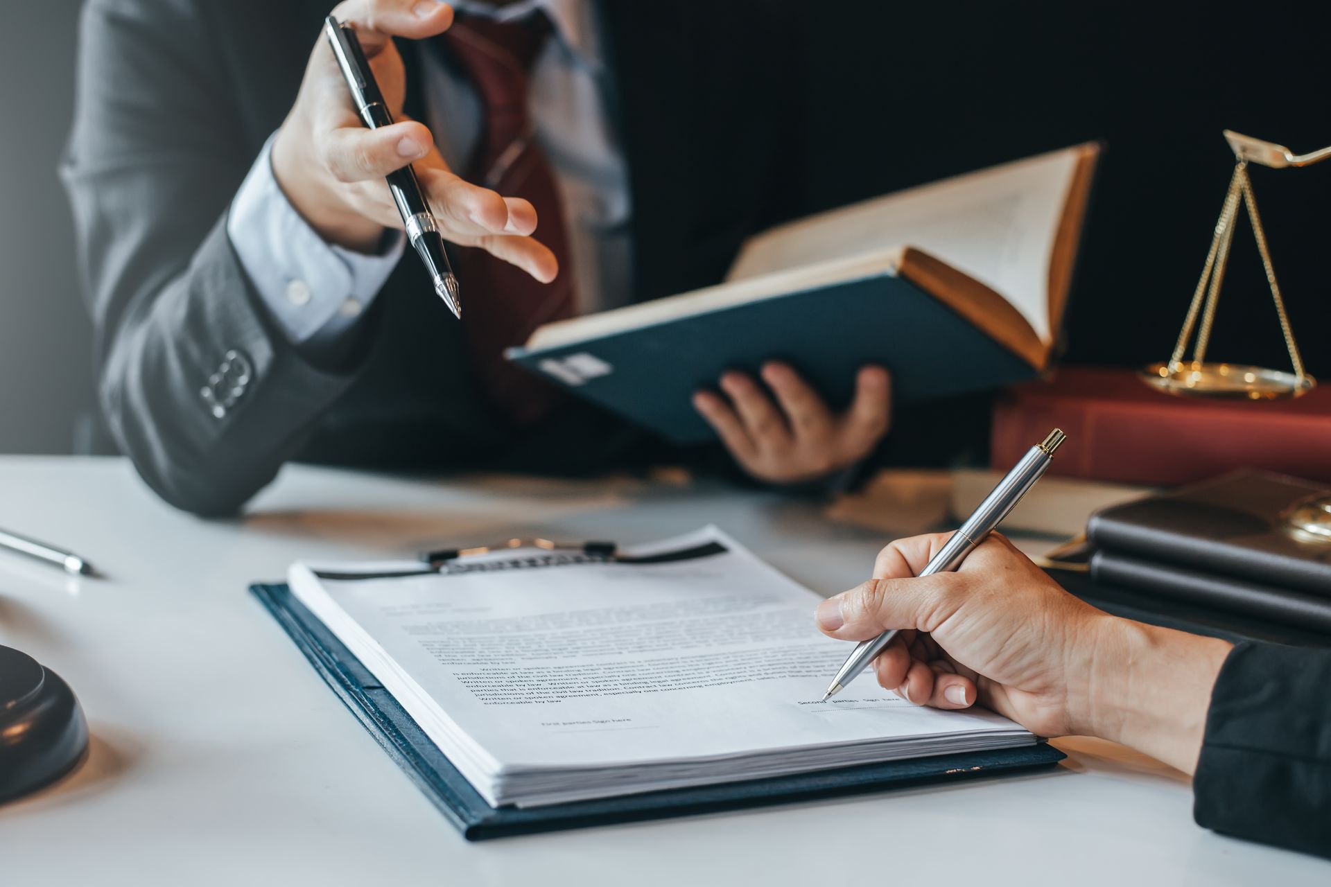Un avocat écrit sur un presse-papiers tandis qu'un autre avocat regarde un livre.