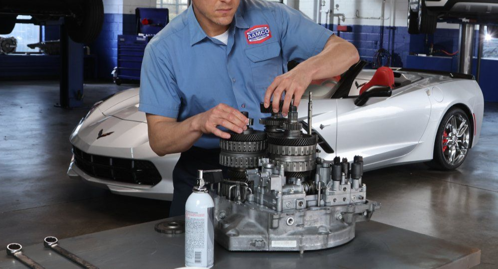 Mechanic inspecting a car engine on a workbench with a silver sports car in the background