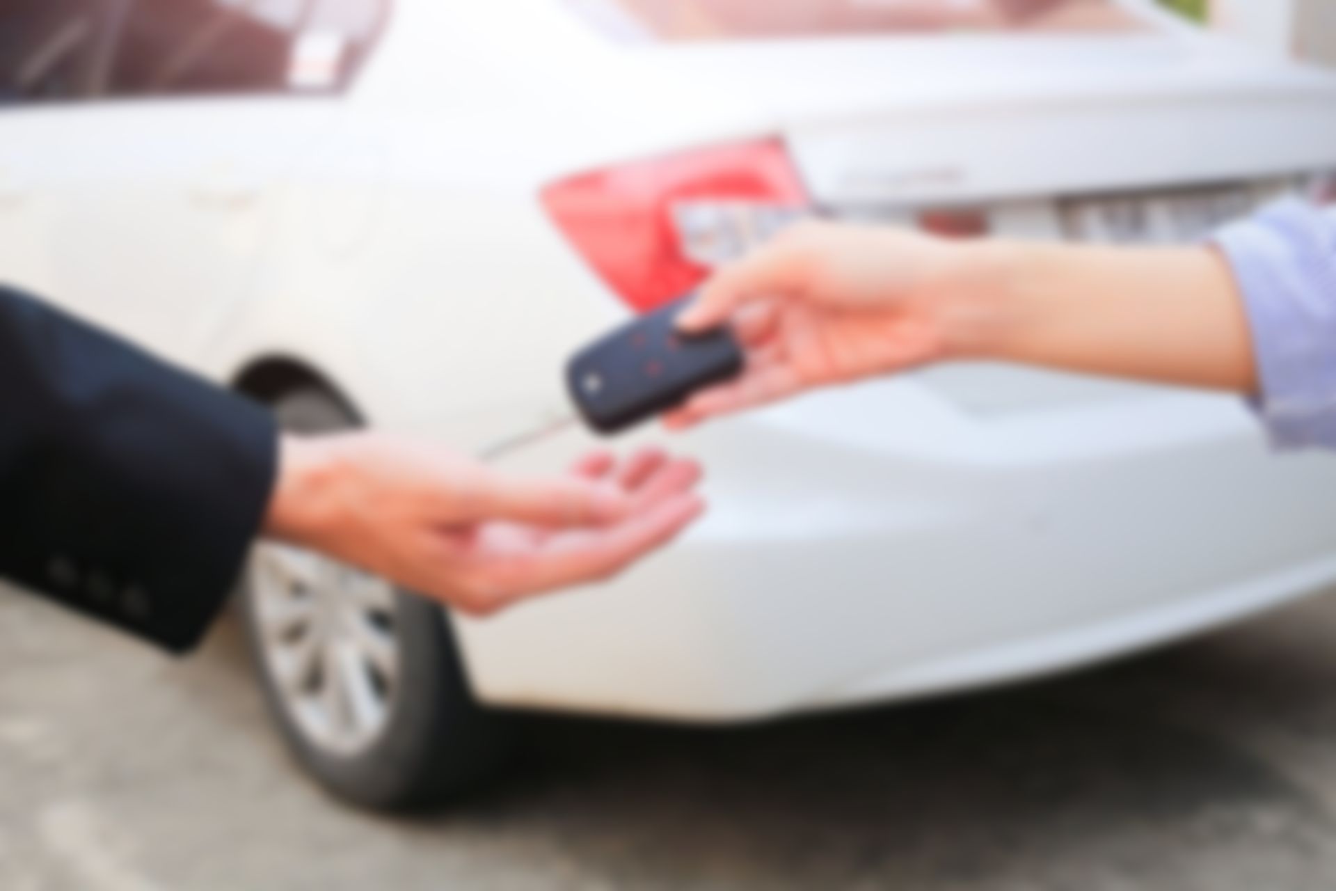 Two people exchange car keys beside a white car.