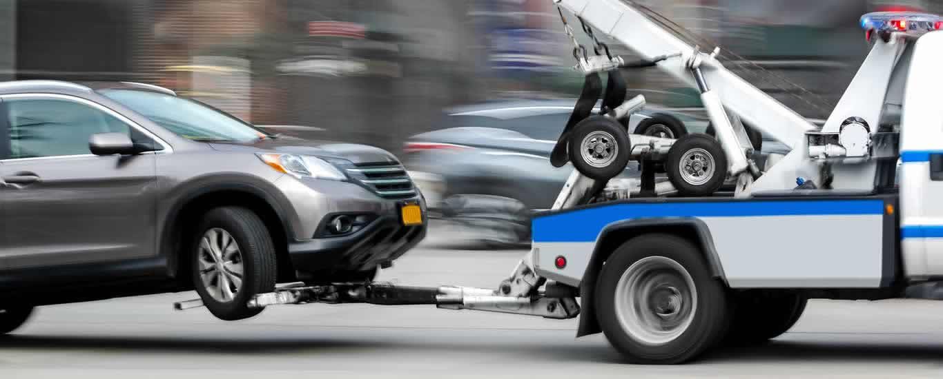 Gray SUV being towed by a blue-and-white tow truck on a city street.