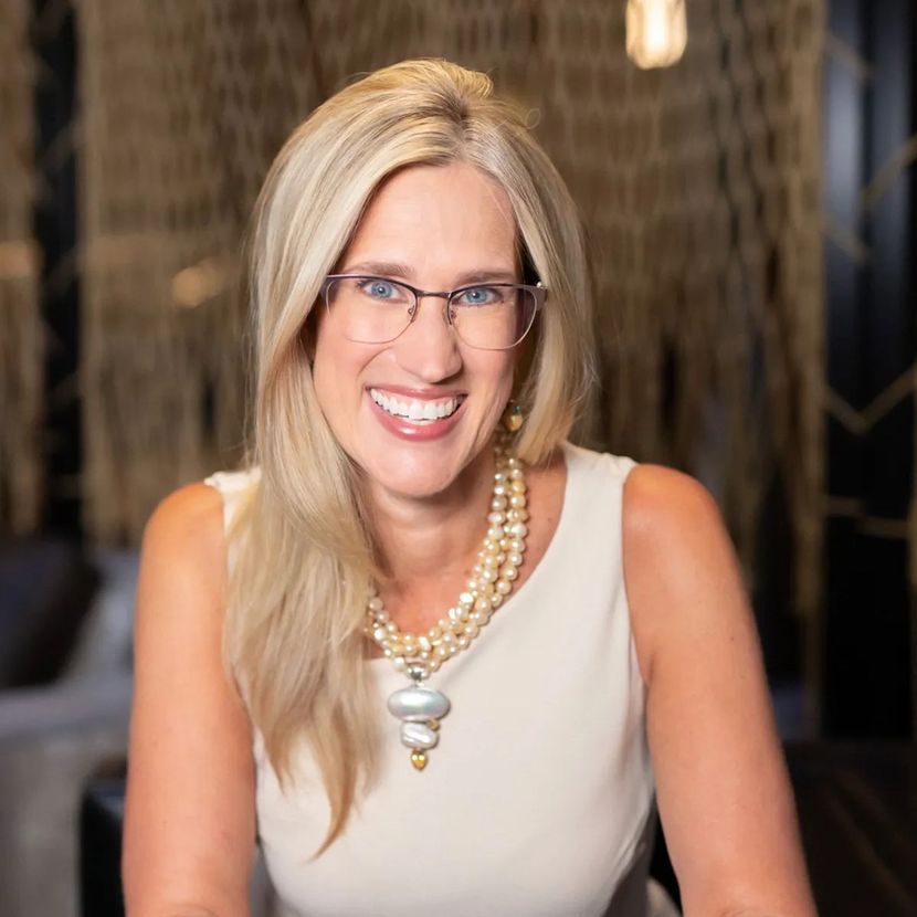 A woman wearing glasses and a pearl necklace smiles for the camera