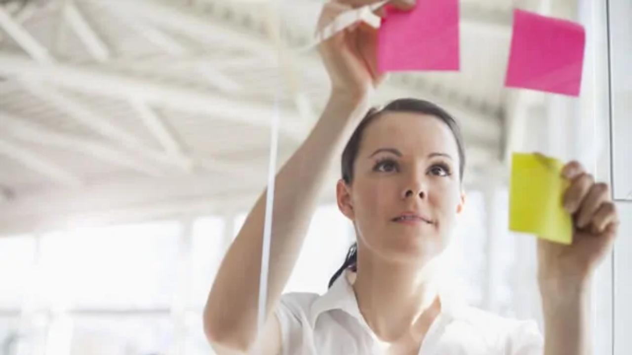 A woman is looking at sticky notes on a glass wall.