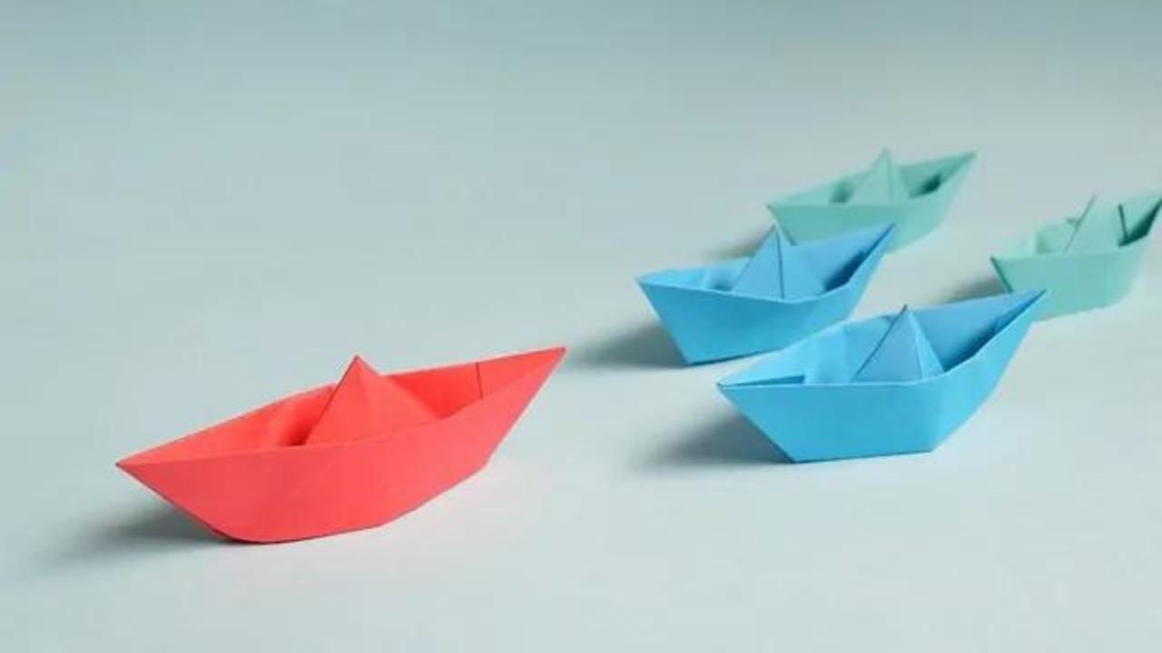 A red paper boat is leading a row of blue paper boats.