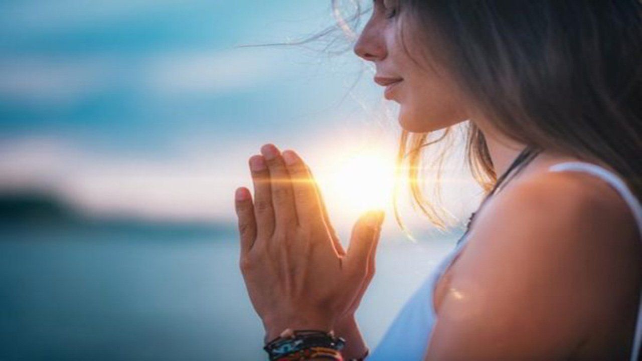 A woman is praying with her hands folded in front of the sun.