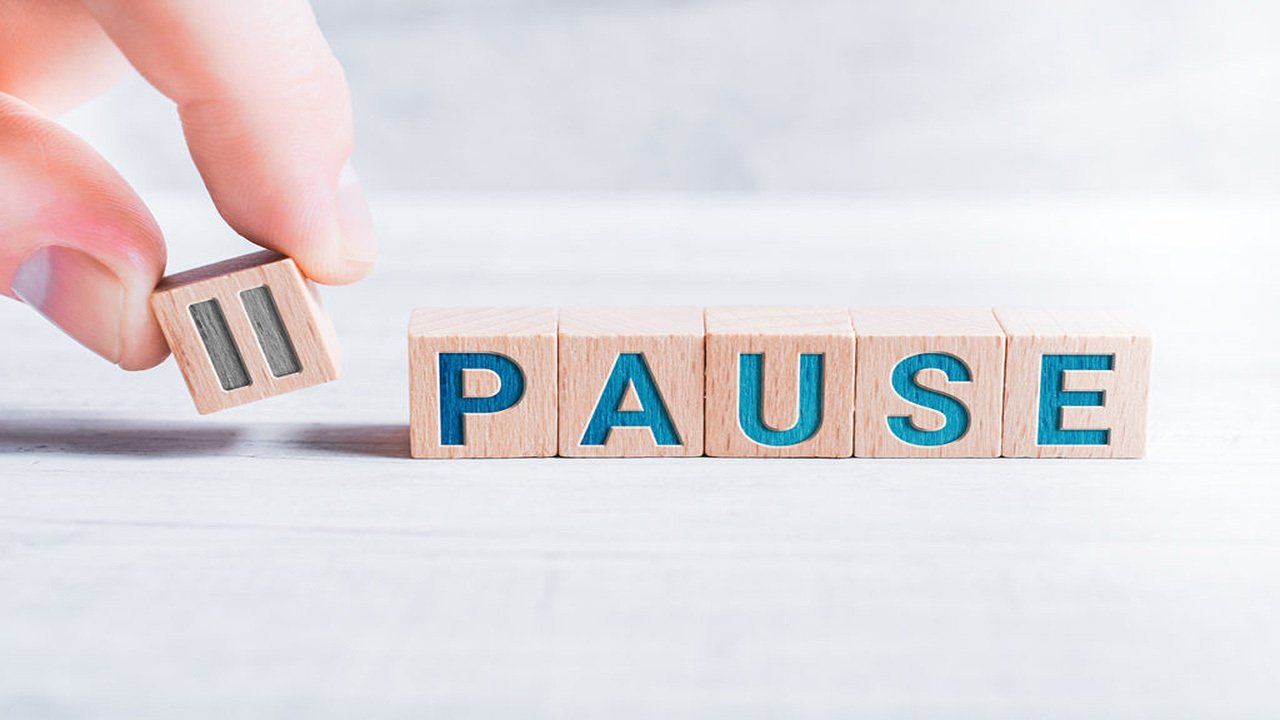 A person is holding a wooden block with the word pause written on it.