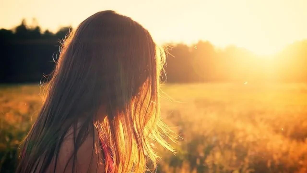 A woman is standing in a field at sunset looking at the sun.