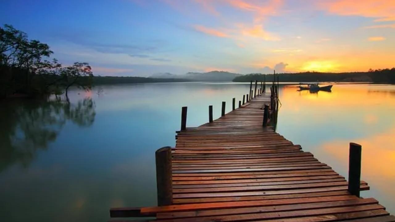 A wooden dock leading into a lake at sunset.