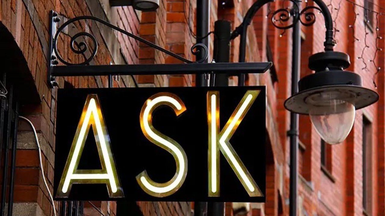 A sign that says ask is hanging from a street light.