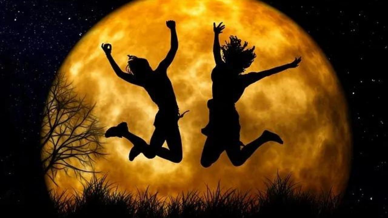 Two people are jumping in the air in front of a full moon.