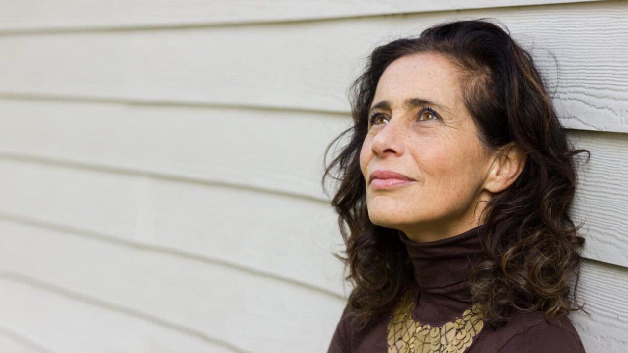 A woman is leaning against a white wall and looking up.
