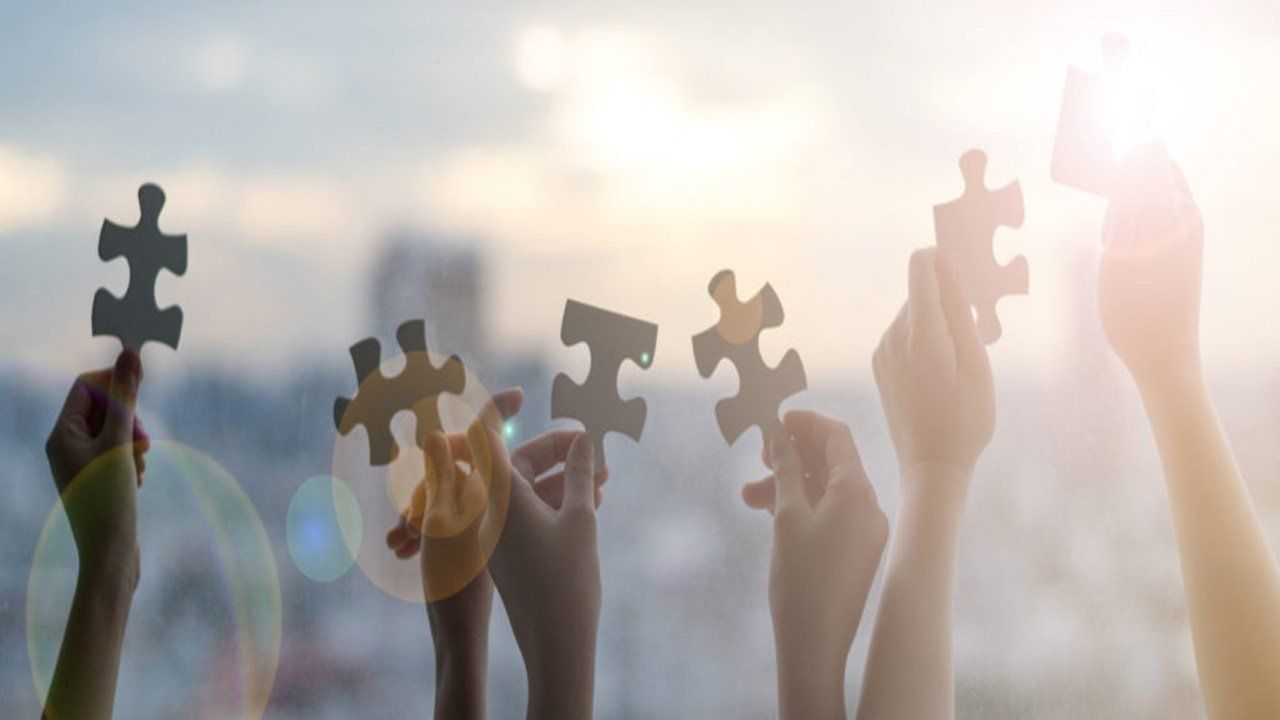 A group of people are holding up puzzle pieces in their hands.