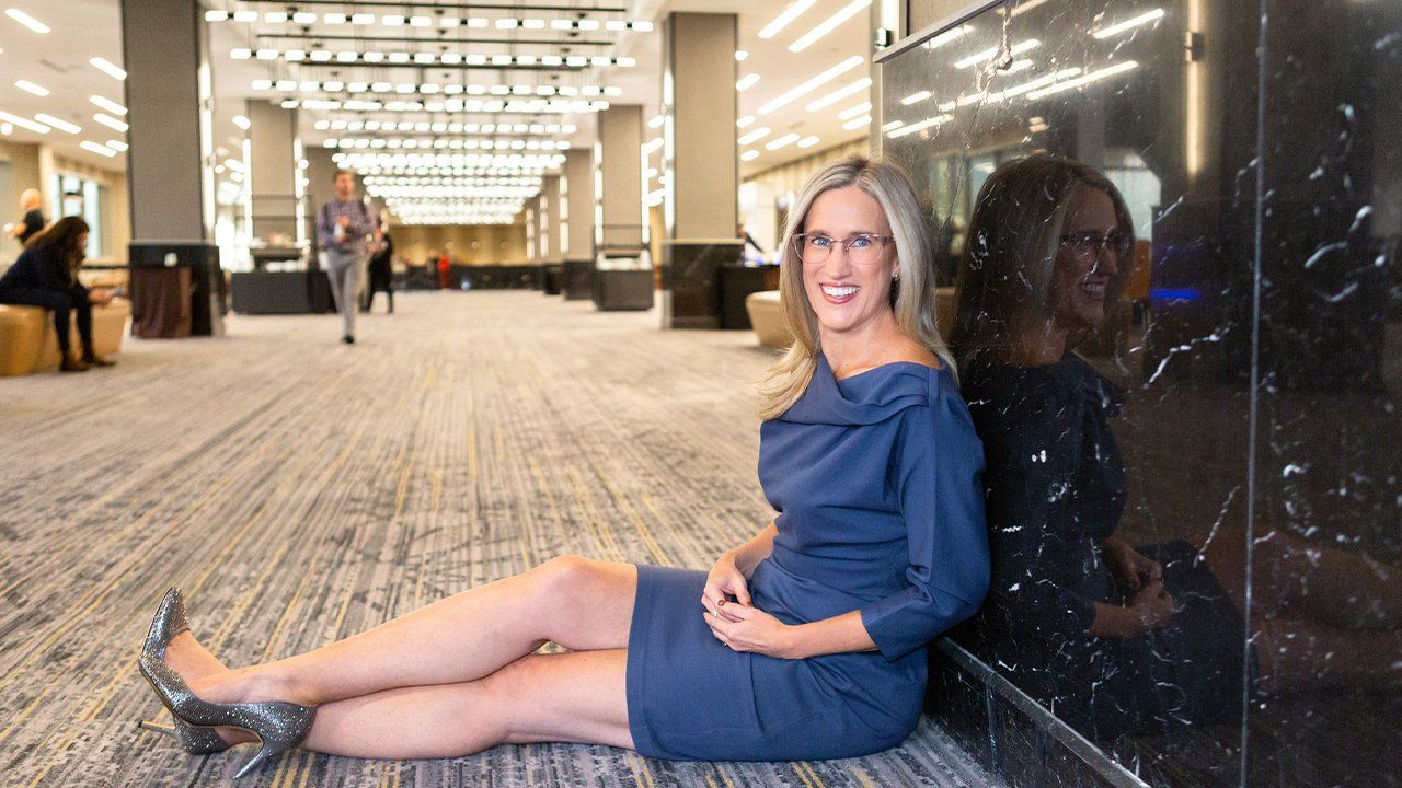 A woman in a blue dress is sitting on the floor in a hallway.