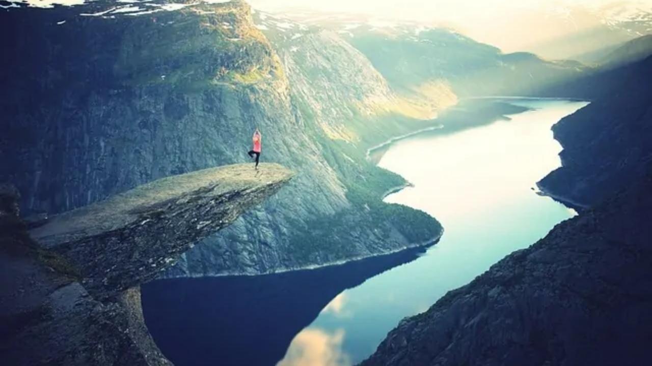 A person is standing on the edge of a cliff overlooking a lake.