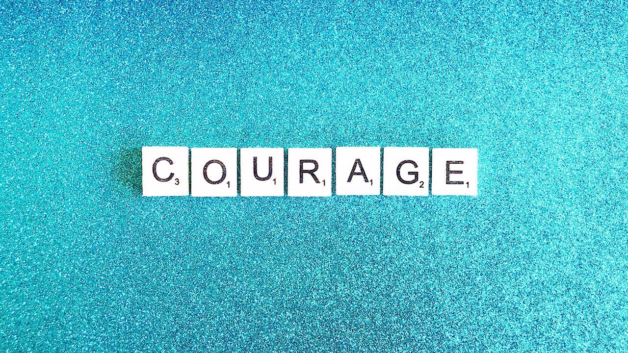 The word courage is written in scrabble tiles on a blue background.
