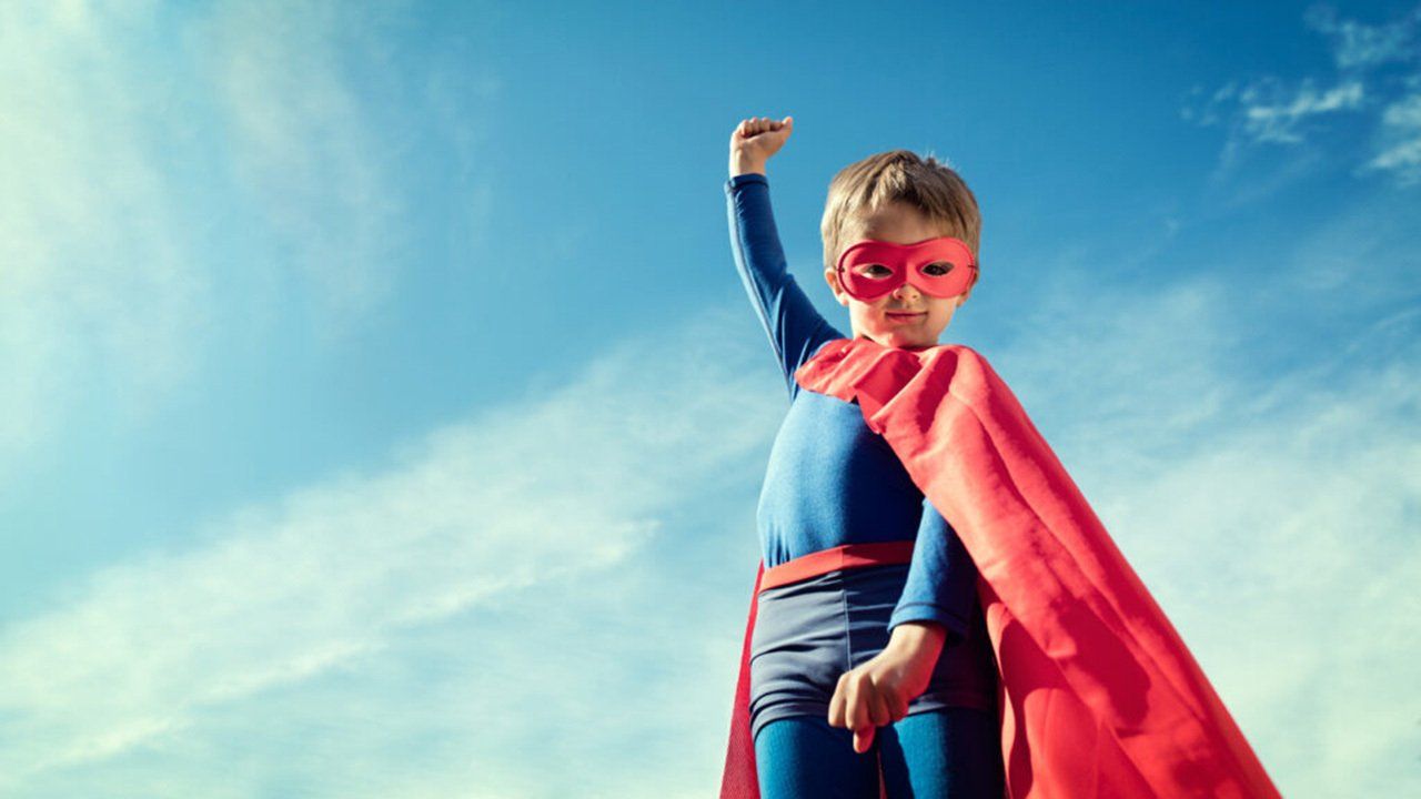A young boy dressed as a superhero with a red cape and mask.