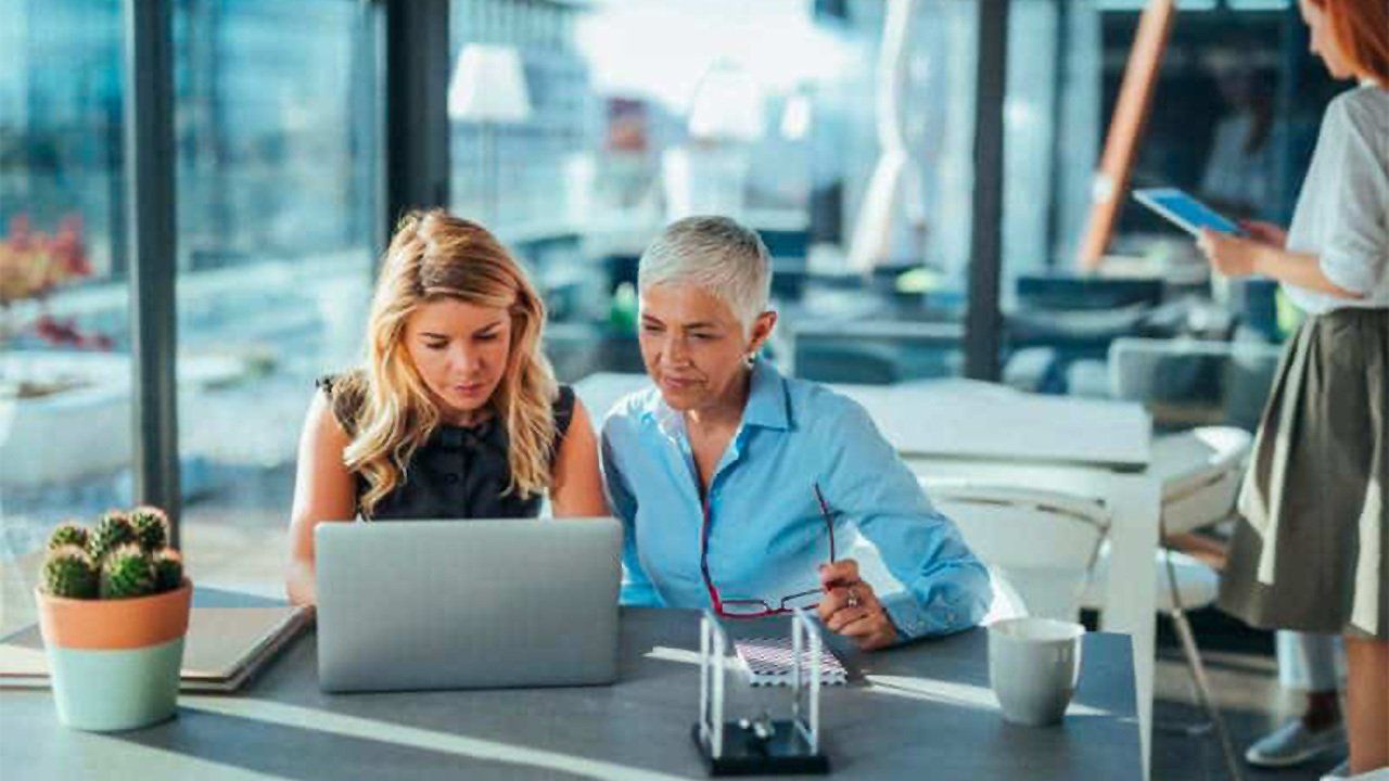 Two women are sitting at a table looking at a laptop computer.