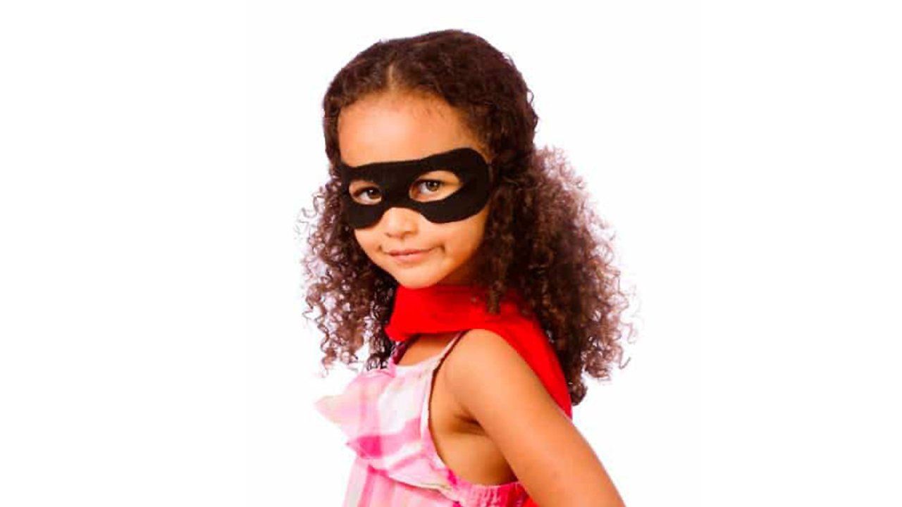 A little girl is wearing a black mask and a red cape.