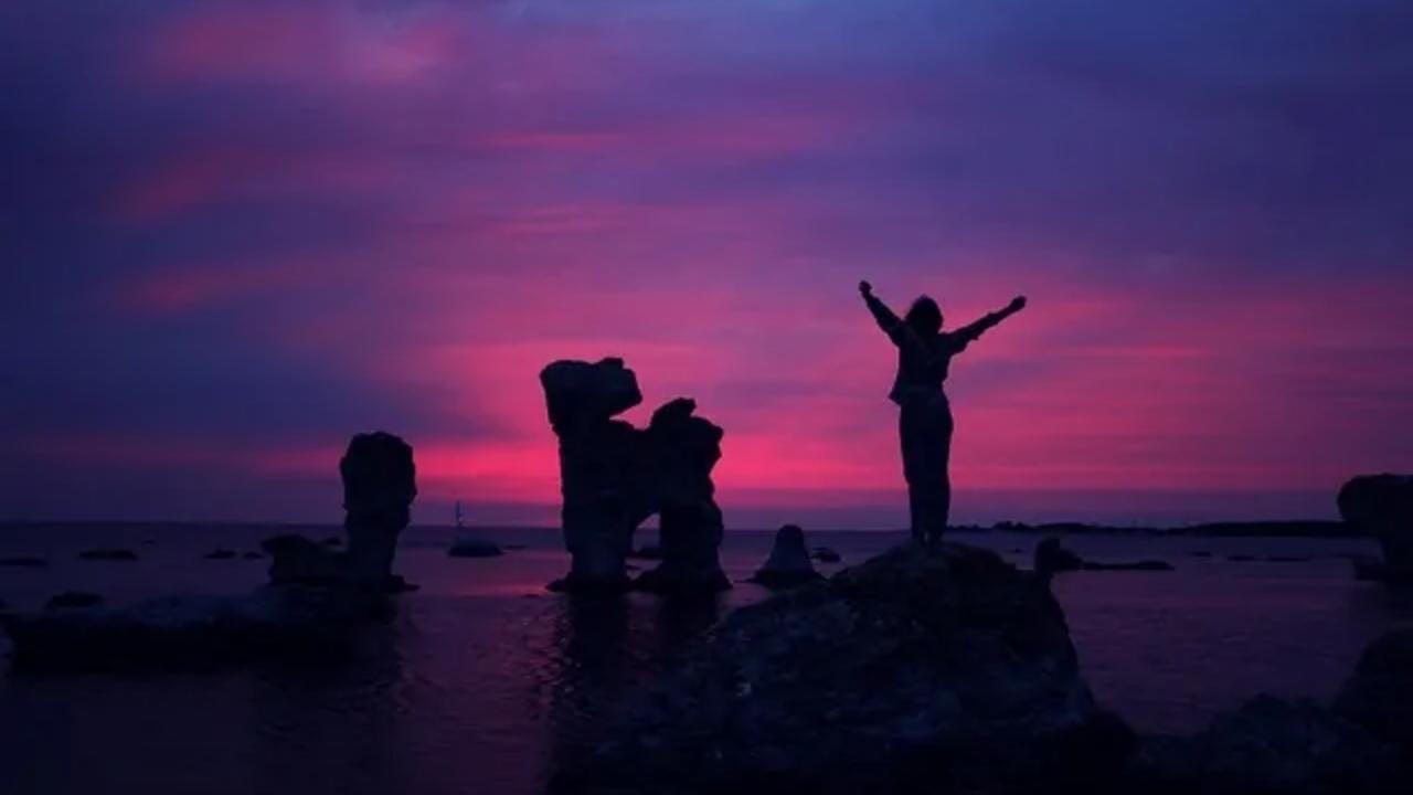 A group of people are standing on top of a rock near the ocean at sunset.