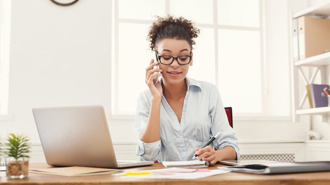 A woman is sitting at a desk talking on a cell phone.