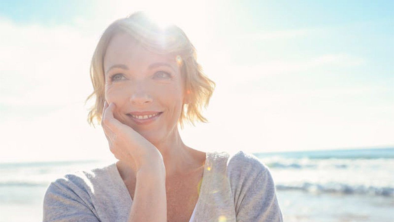 A woman is smiling on the beach with the sun shining on her face.