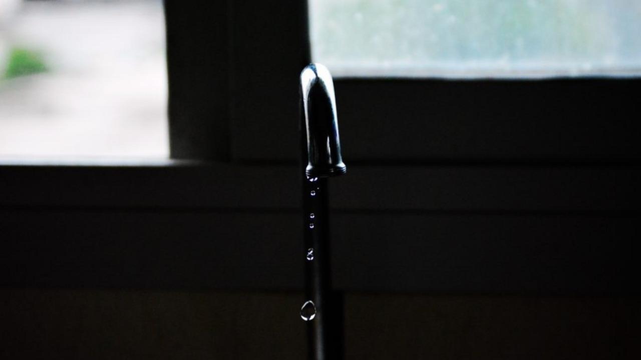 A close up of a faucet with water running out of it in front of a window.