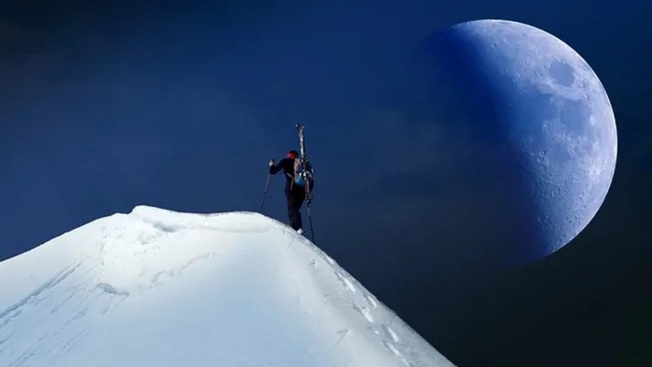 A person is standing on top of a snow covered mountain with the moon in the background.