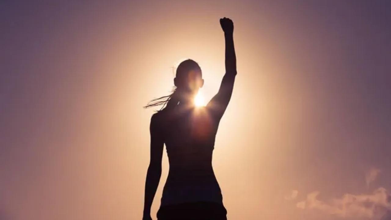 A woman is raising her fist in the air in front of the sun.