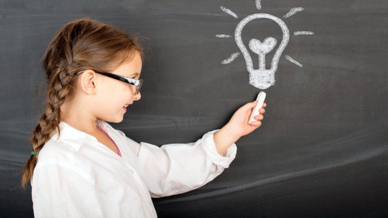 A little girl is drawing a light bulb on a blackboard.