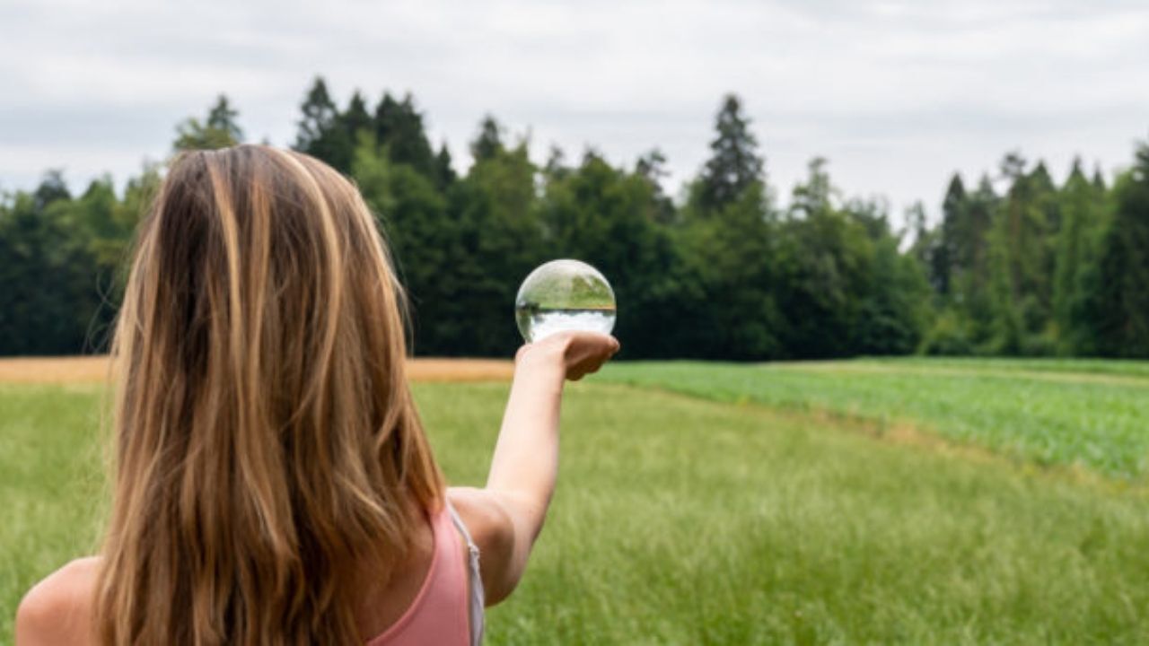 A young girl is holding a glass ball in a field.