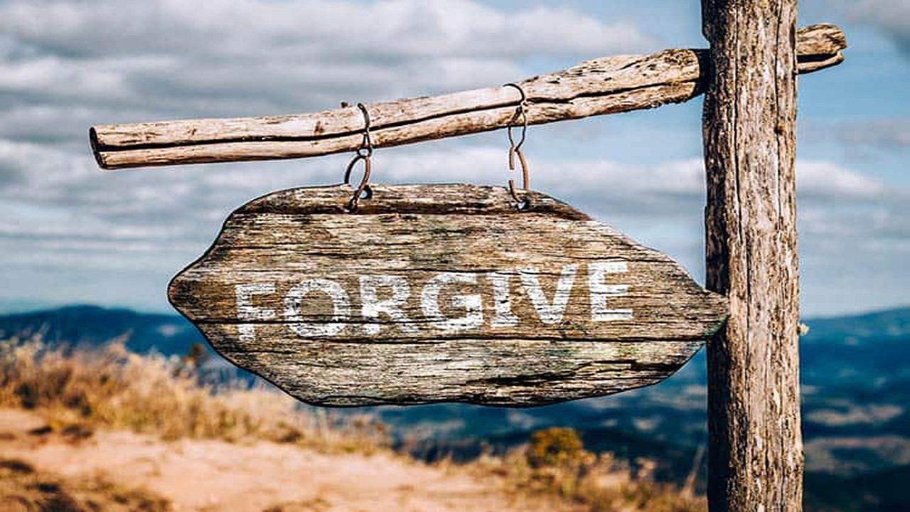 A wooden sign with the word forgive written on it is hanging from a wooden post.