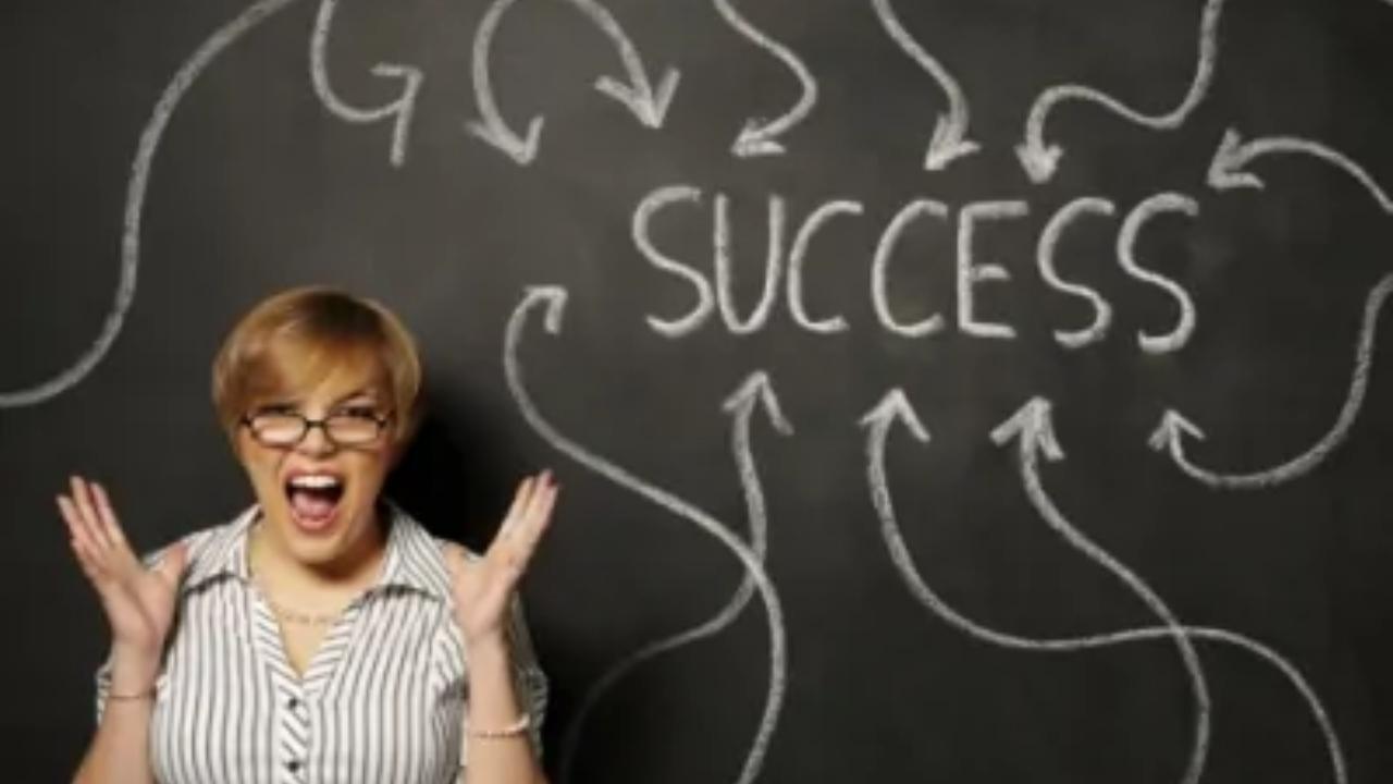 A woman is standing in front of a blackboard with the word success written on it