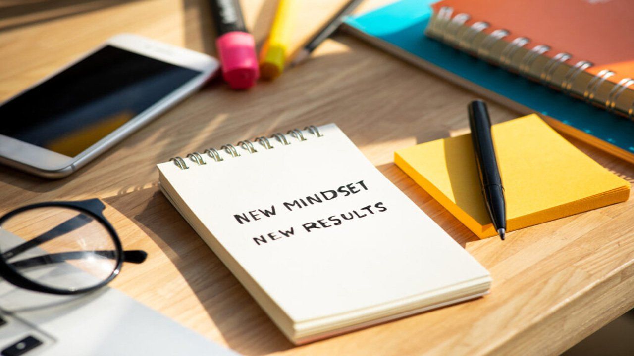 A notebook with the words `` new mindset new results '' written on it is sitting on a wooden table.