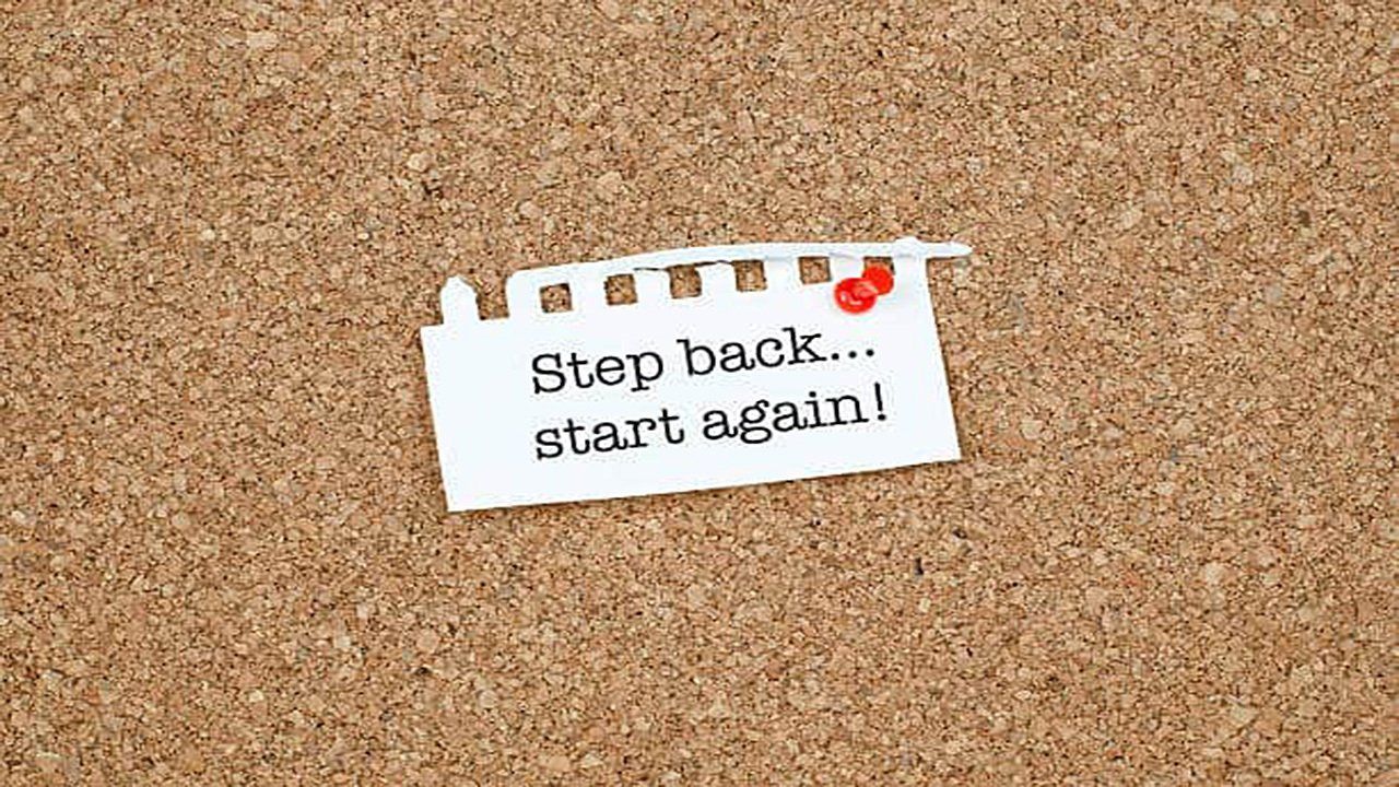 A piece of paper that says step back start again is pinned to a cork board.