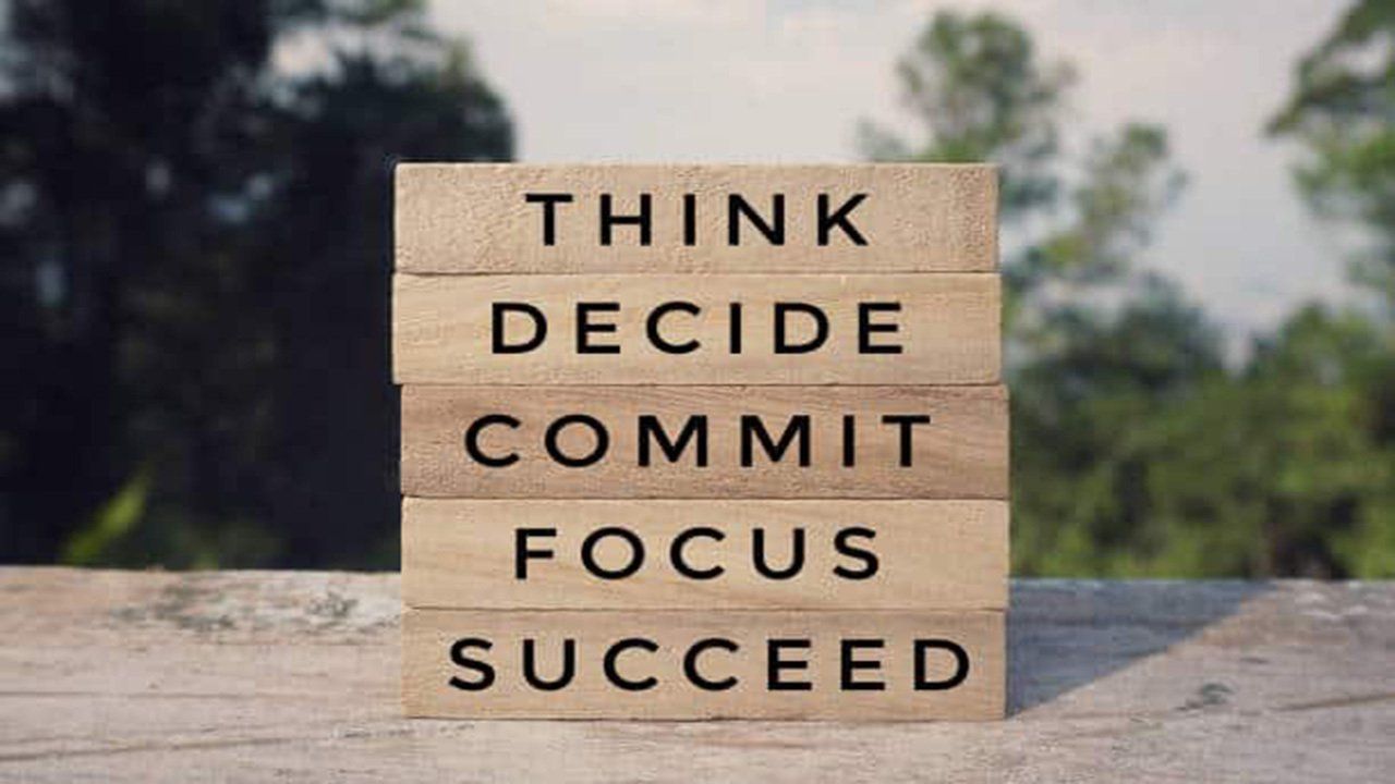 A stack of wooden blocks with the words think decide commit focus succeed written on them.