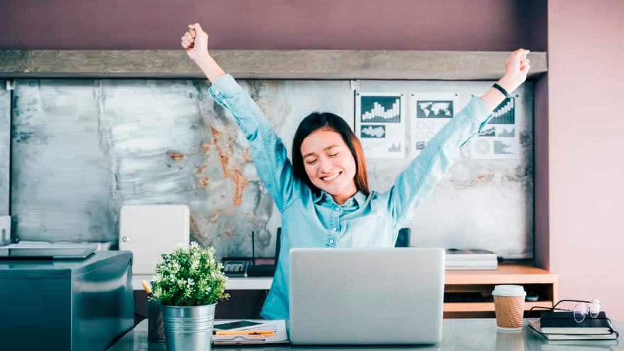 A woman is sitting in front of a laptop computer with her arms in the air.