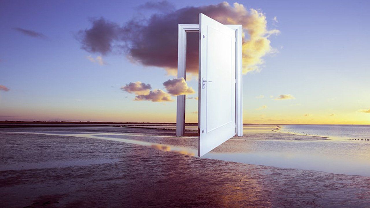 An open door is leading to the ocean at sunset.