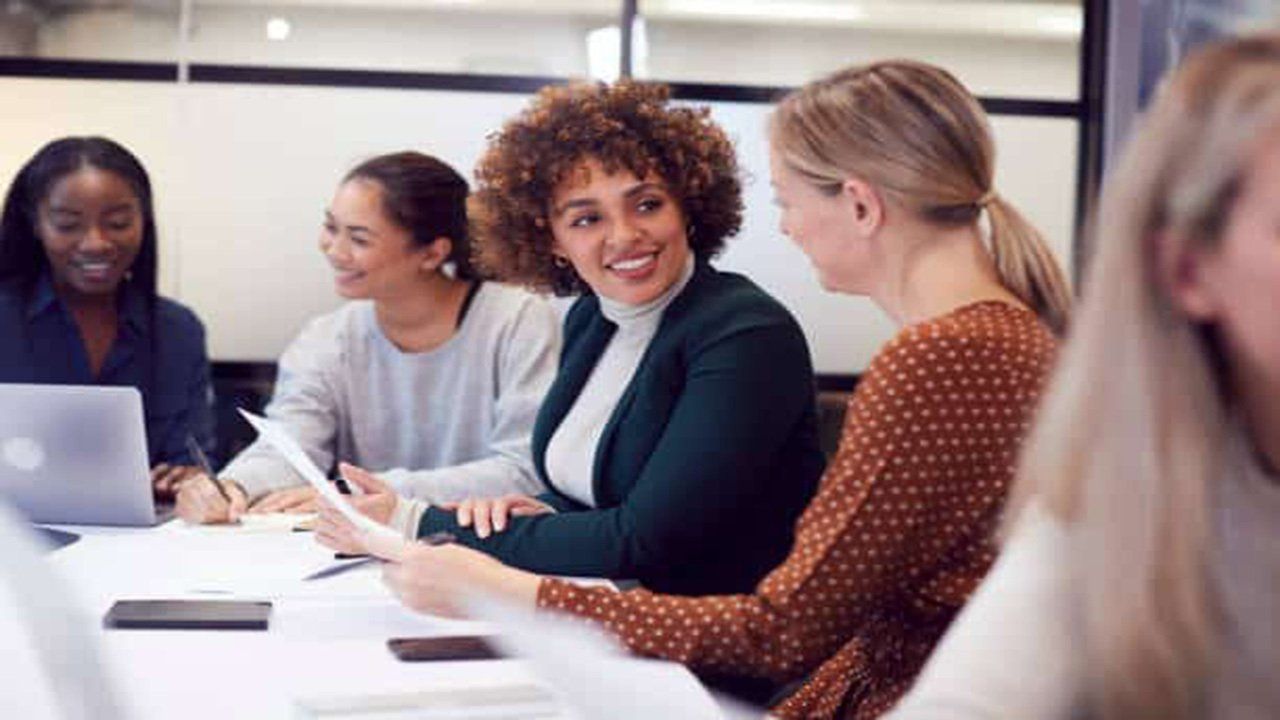 A group of women are sitting around a table with laptops.