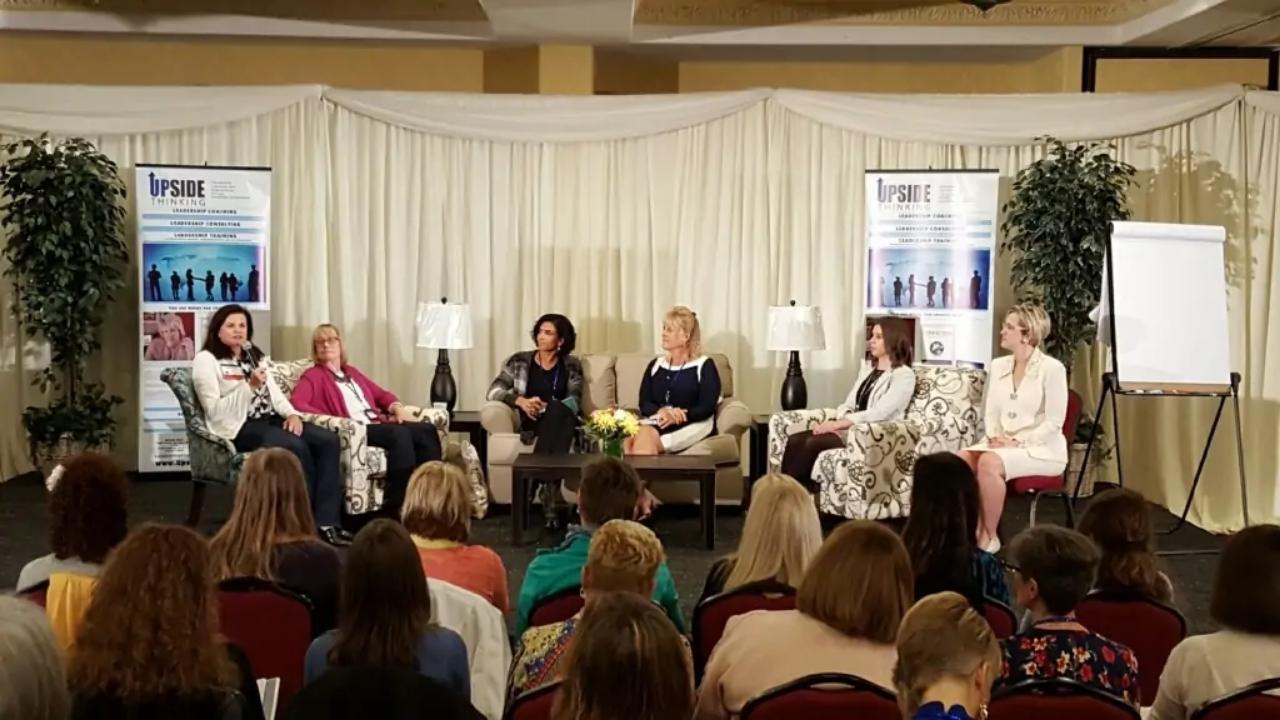 A group of women are sitting in chairs in front of a stage.