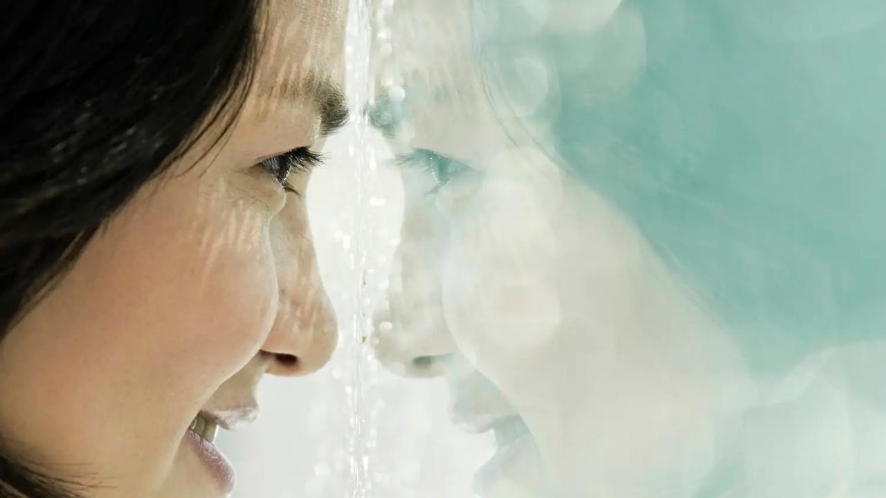 A woman is looking at her reflection in a mirror.
